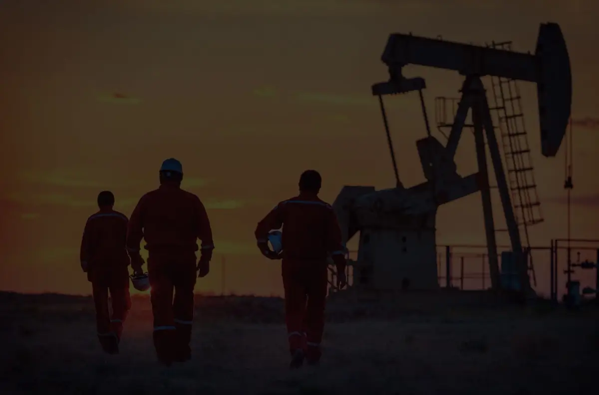 men walking towards an pump jack at sunset.